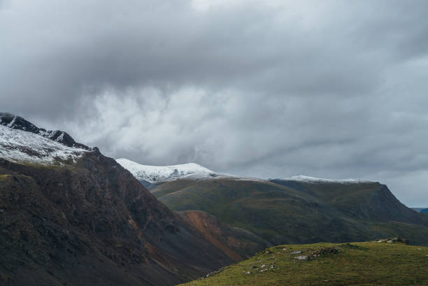 istock Atmospheric alpine landscape with deep gorge and snow-capped multicolor mountains in overcast weather. Beautiful scenery with snowbound mountain range under cloudy sky. Motley high mountains with snow 1347369278
