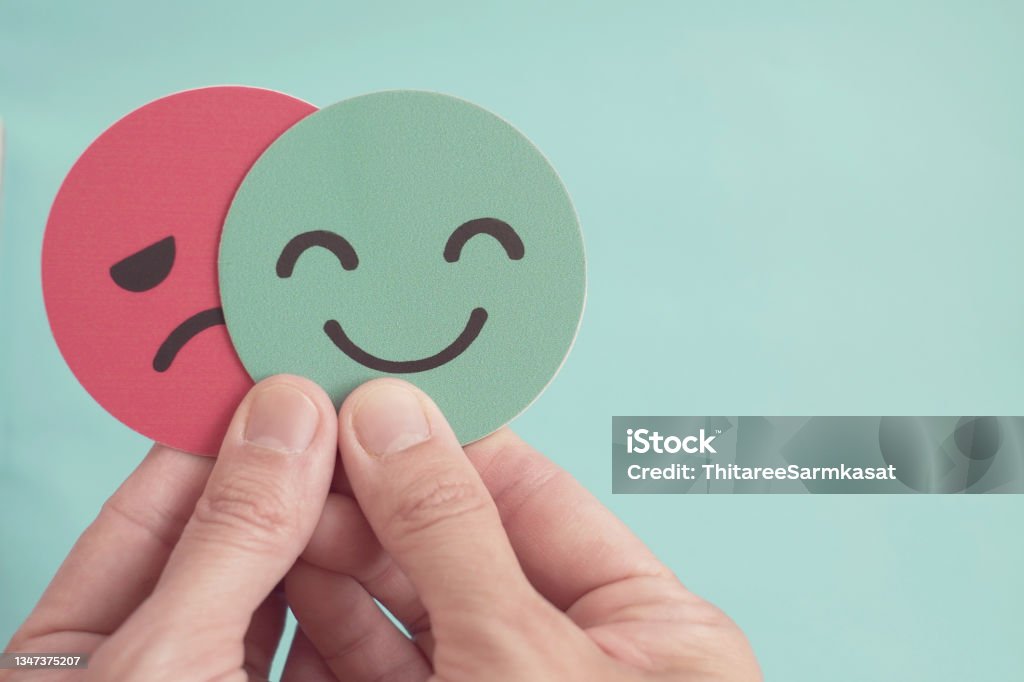 Hands holding sad face hiding behind happy face, bipolar and depression, mental health, split personality,  mood change, Emotion Stock Photo