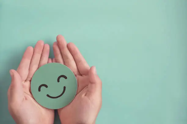 Photo of Hands holding green happy smile face paper cut, good feedback rating and positive customer review, experience, satisfaction survey ,mental health assessment, child wellness,world mental health day concept