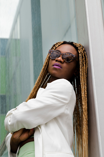 Portrait of empowered african american young woman wearing sunglasses looking at camera with a daring attitude. Long blond braided hairstyle.