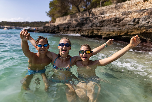 Brothers and sister are having fun in the sea. Kids are floating in the beautiful cove on the shores of Majorca, Spain\nSunny summer day.\nCanon R5