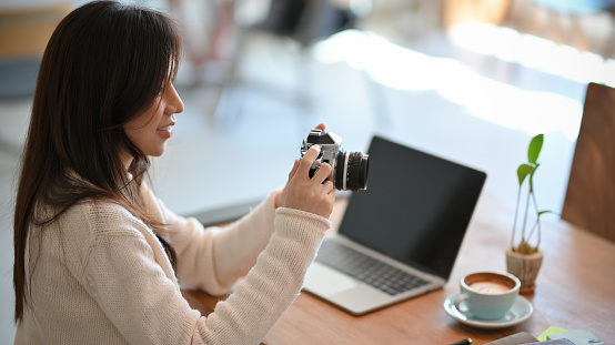 Beautiful young asian female freelancer photographer, web blogger looking a photo in camera at co-working space