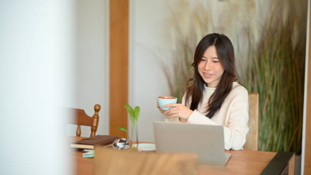 istock Charming young woman working on her laptop computer while sipping warm coffee 1347408129