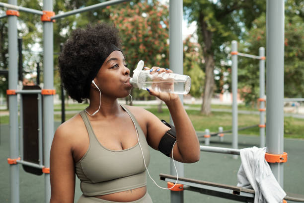 istock Young thirsty woman in tracksuit drinking water from plastic bottle 1347413440