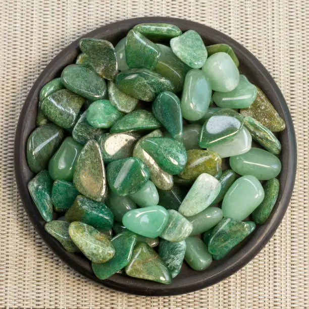 Macroshooting of natural mineral rock specimen - tumbled green aventurine gemstone isolated on grey textured background front view partial focused Narrow focus line, shallow depth of field