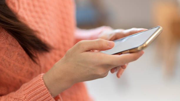 istock Female in pink sweater holding, using modern smart mobile phone, blurred background. 1347413860