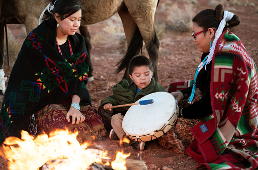 Navajo siblings warming up around campfire at sunset on Monument Valley - Arizona
