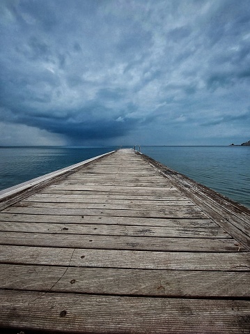 A wide shot of a wooden pedestrian deck reaching out into the blue sea. The sky is loaded with dark clouds. The shot is taken in October by the Marmara sea in northwest Turkey.