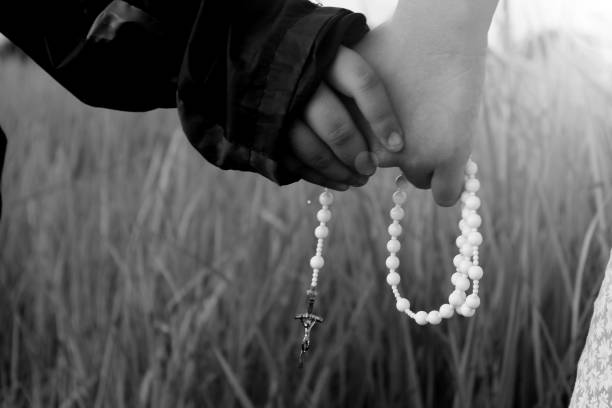 Two kids holding hands with Rosary in hands in monochrome black and white backgrounds. Children praying rosary, the catholic symbol of faith concept.