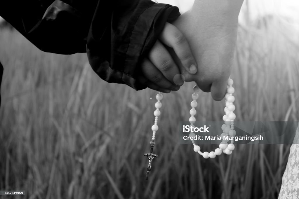 Children holding Rosary in hands. Two kids holding hands with Rosary in hands in monochrome black and white backgrounds. Children praying rosary, the catholic symbol of faith concept. Virgin Mary Stock Photo