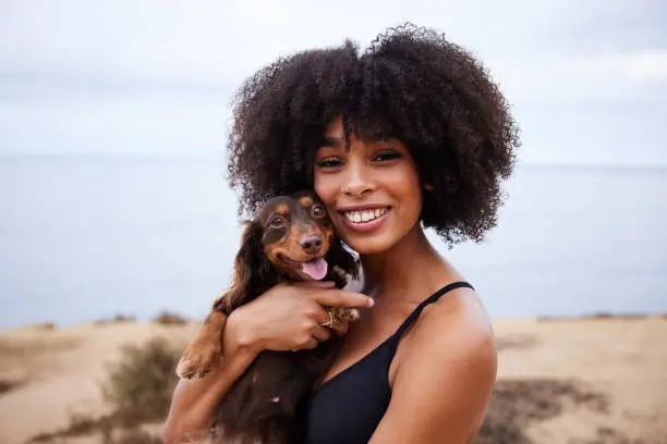 Photo of Smiling young woman holding her cute little dachshund by the ocean