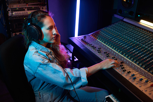 Young woman wearing headphones listening to music and typing on music keyboard to record a song