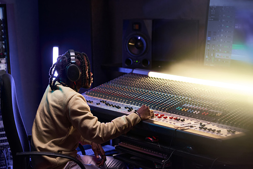 African producer in headphones using music keyboard to write a new song in the recording studio