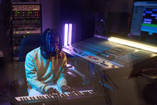 African musical producer playing electric piano and writing music in the recording studio