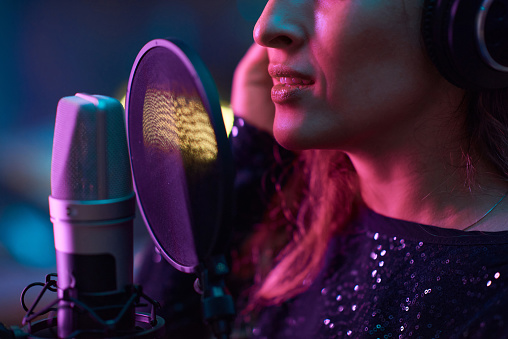 Close-up of young singer singing to microphone while recording a new song in the studio