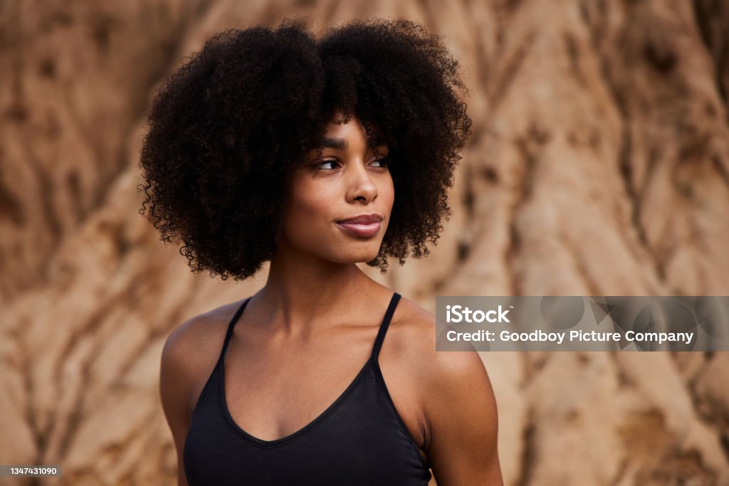 Fit woman standing outdoors after a late afternoon trail run Smiling young African American woman in sportswear glancing sideways during a break from a run outdoors Women Stock Photo