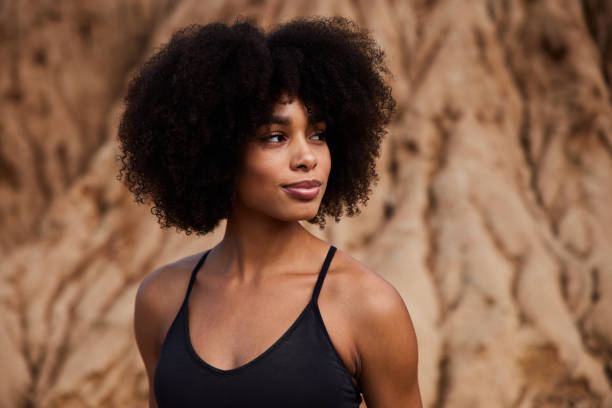 Fit woman standing outdoors after a late afternoon trail run Smiling young African American woman in sportswear glancing sideways during a break from a run outdoors beautiful woman summer stock pictures, royalty-free photos & images