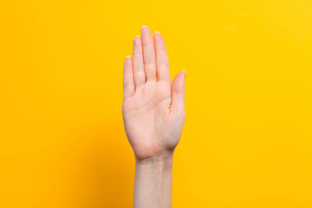 Female hand and gesture for a stop or hello. Yellow background. Close up. Copy space.