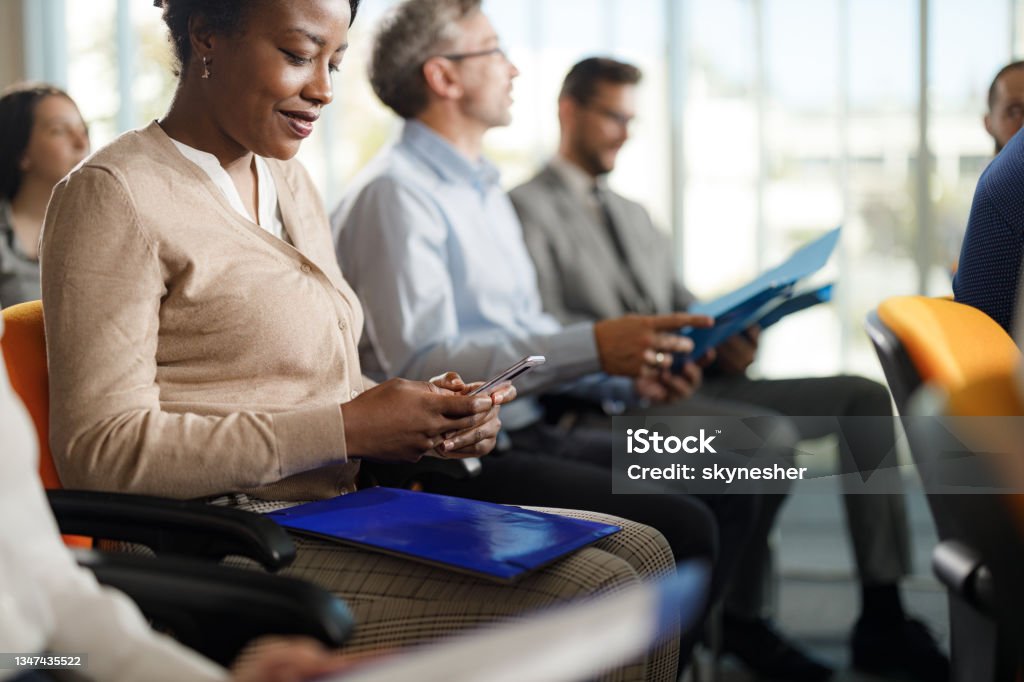 Smiling black businesswoman using cell phone on a seminar. Smiling African American businesswoman using mobile phone on education event in board room. Online Messaging Stock Photo
