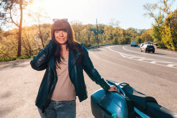 концепция всемирного дня мотоциклистов. счастливая молодая женщина в кожаной куртке и солнцезащитных очках позирует возле мотоцикла - motorcycle women tattoo sensuality стоковые фото и изображения