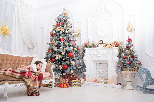 Morning before christmas. Little girl lay on couch near christmas tree beautiful interior. Magical moment. Excited before christmas night. Happy new year. Family holiday. Christmas tree and presents.