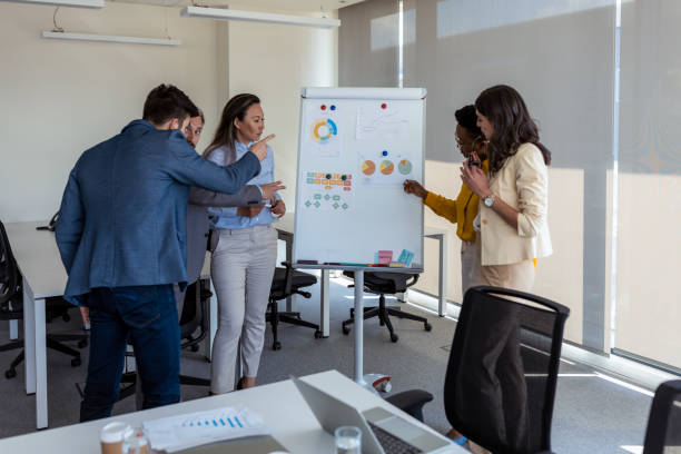 istock Working as team. Diverse group of focused businesspeople brainstorming together on a whiteboard during a strategy session in a bright modern office 1347449496