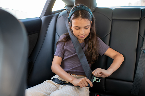 Adorable colegiala abrochándose el cinturón de seguridad mientras está sentada en el coche photo