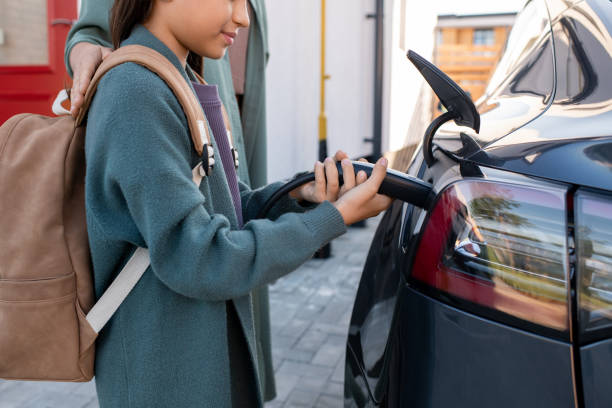 istock Adorable girl with backpack helping to charge electric car 1347452321