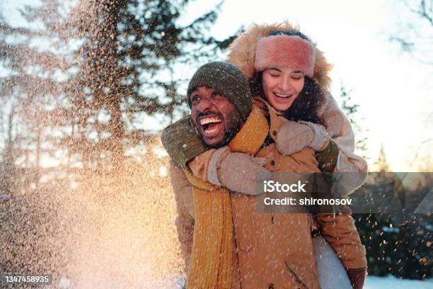 Cheerful Multiracial Couple In Winterwear Laughing While Girl Embracing Her Boyfriend Stock Photo - Download Image Now
