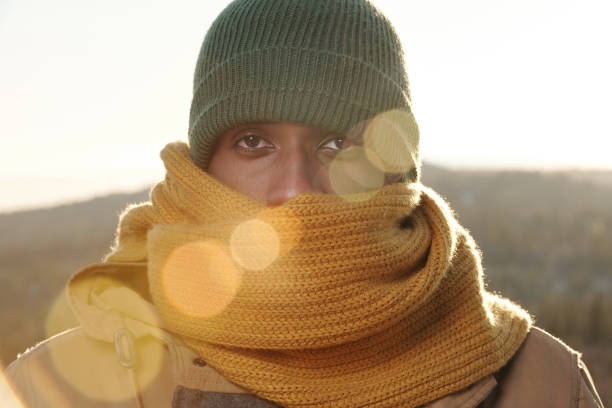 Frozen young man of African ethnicity in knitted scarf and cap looking at camera
