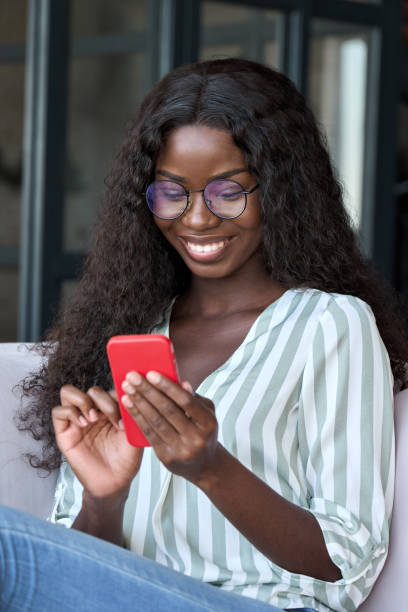 istock Young happy black African woman using mobile app on cell phone sitting on couch. 1347465732