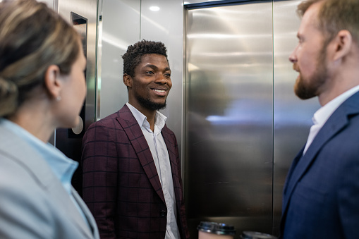 Happy young African businessman smiling while looking at male colleague during communication inside elevator