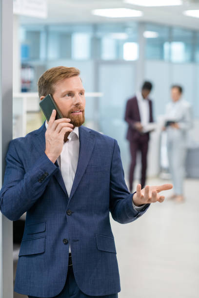 istock Bearded businessman communicating on smartphone against two colleagues 1347466003