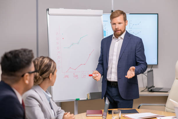 istock Young confident businessman with red highlighter discussing financial garph with colleagues 1347466065