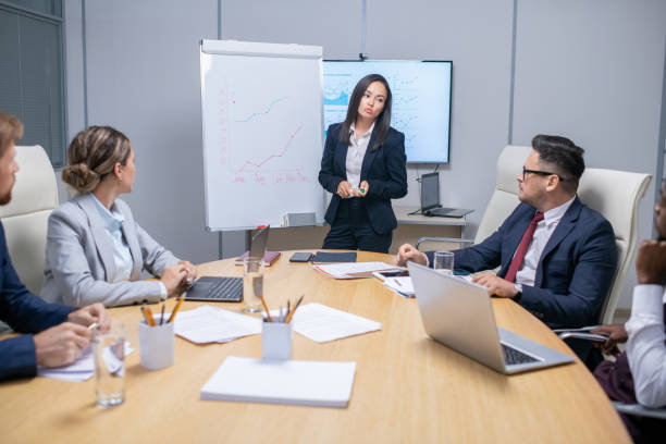 istock Young female broker standing by whiteboard with graph during presentation 1347466089