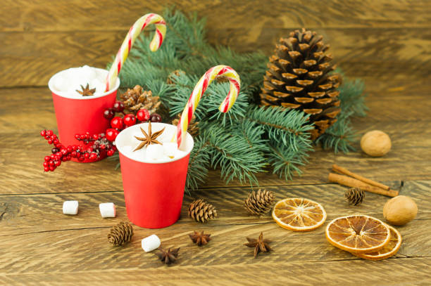 istock New Year's composition on a wooden background. two paper red cups with coffee and marshmallows, caramel, blue spruce branches and a cedar cone. 1347473954