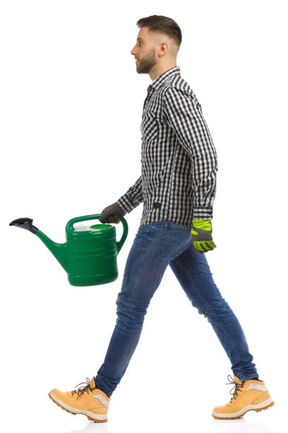 istock Young man is walking with green watering can. Side view. Studio shot, isolated. 1347473993
