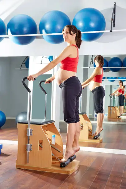 pregnant woman pilates tendon stretch exercise in wunda chair at gym indoor