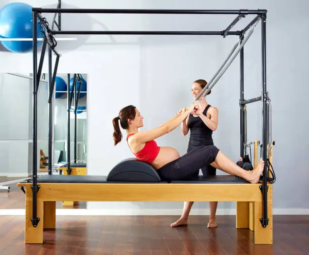 pregnant woman pilates reformer roll up cadillac exercise with personal trainer