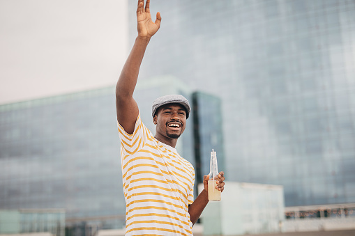 One man, young black male waving and holding bottle of soda in city.