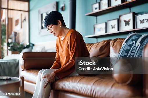 istock A distraught senior Asian woman feeling unwell, suffering from pain in leg while sitting on sofa in the living room at home 1347484703
