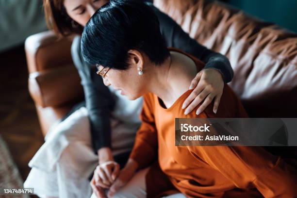 A Daughter Embraces Her Elderly Mother Who Is Feeling Unwell Holding Her Mothers Hand Giving Support And Consoling Her While Sitting On Sofa In The Living Room At Home Stock Photo - Download Image Now