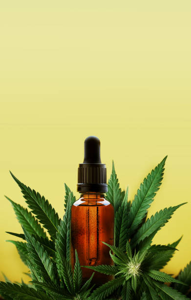 Glass dropper bottle of cannabis oil with marijuana plants and yellow background stock photo