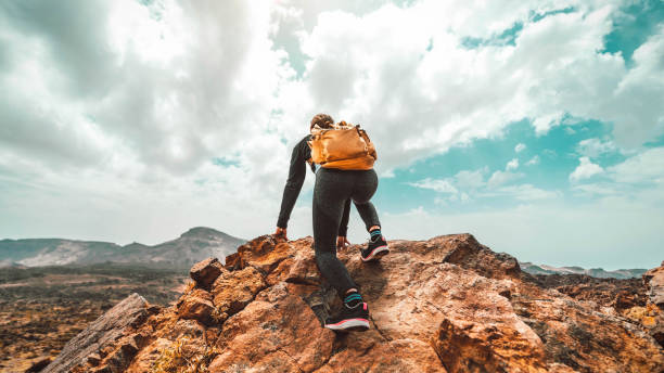 mujer con mochila senderismo montañas - excursionista escalando en la cima del acantilado - deporte, éxito, liderazgo y concepto de estilo de vida - climbing hill fotografías e imágenes de stock
