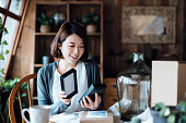 Smiling young Asian woman looking happy as she unboxing the delivered packages from online purchases at home. Online shopping, enjoyable customer shopping experience