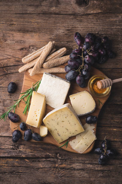 plato de queso. surtido de quesos franceses y piamonteses servidos con miel, uva, grissini y romero sobre el fondo rústico de madera.  entrantes o aperitivos de invierno y otoño - cheese still life tray french cuisine fotografías e imágenes de stock