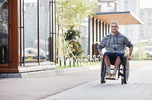 Mature man with disability riding in wheelchair outdoors he walking on fresh air