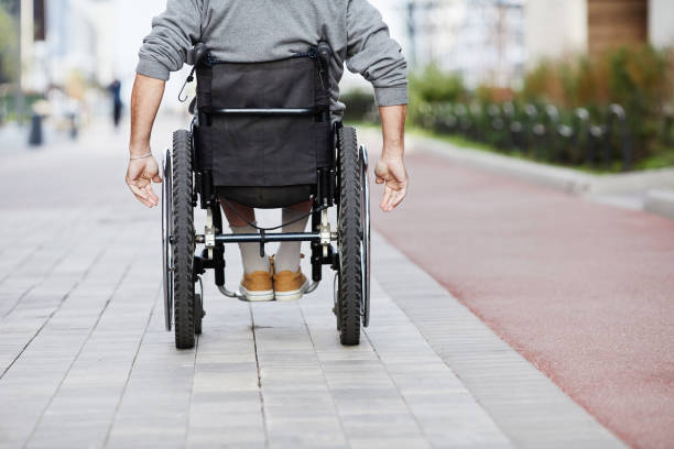 Man in wheelchair riding outdoors Rear view of mature man riding in wheelchair along the street paraplegic stock pictures, royalty-free photos & images