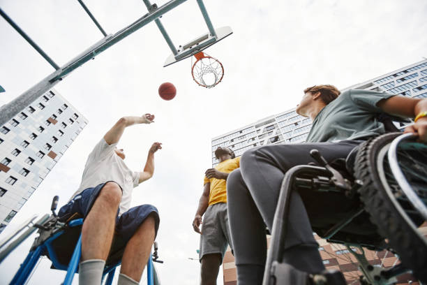 Low angle view of couple in wheelchairs throwing the ball into the basket together with coach outdoors