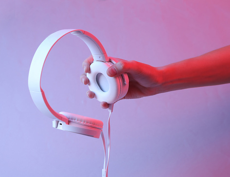 Hand holding white stereo headphones in pink blue neon gradient light
